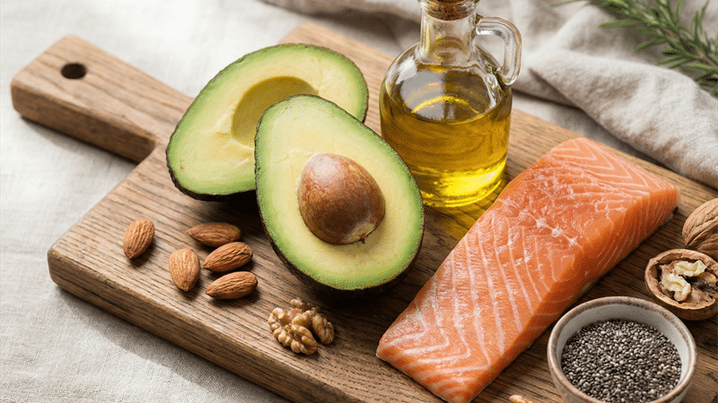 Healthy fats including avocado, salmon, olive oil, and nuts that fuel red light therapy sessions